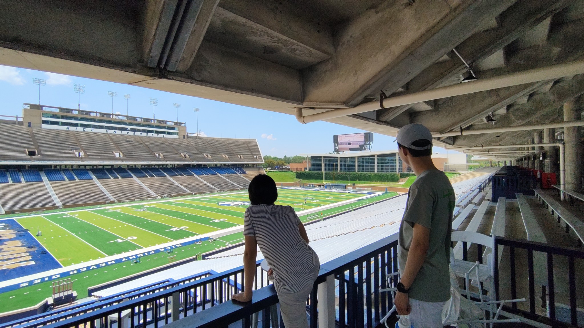 Two people standing before a stadium football field, hearing a recording of JFK played back through the speakers